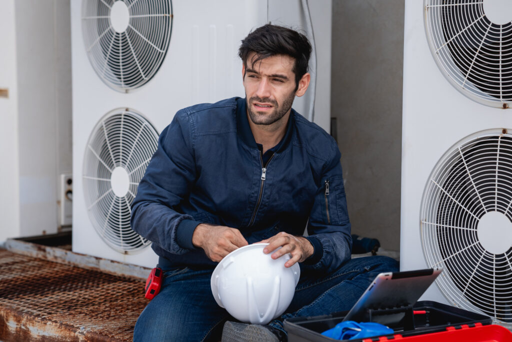 HVAC technician with a hard hat in Phoenix, AZ, sitting near AC units. Home AC repair and maintenance for residential and commercial buildings.
