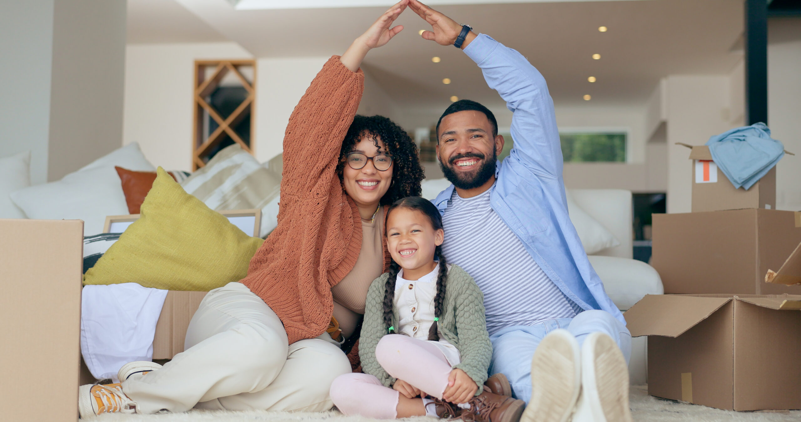 Happy family in new home, Phoenix, AZ. Parents make roof shape with arms. Cooling system ensures comfort in their new house.
